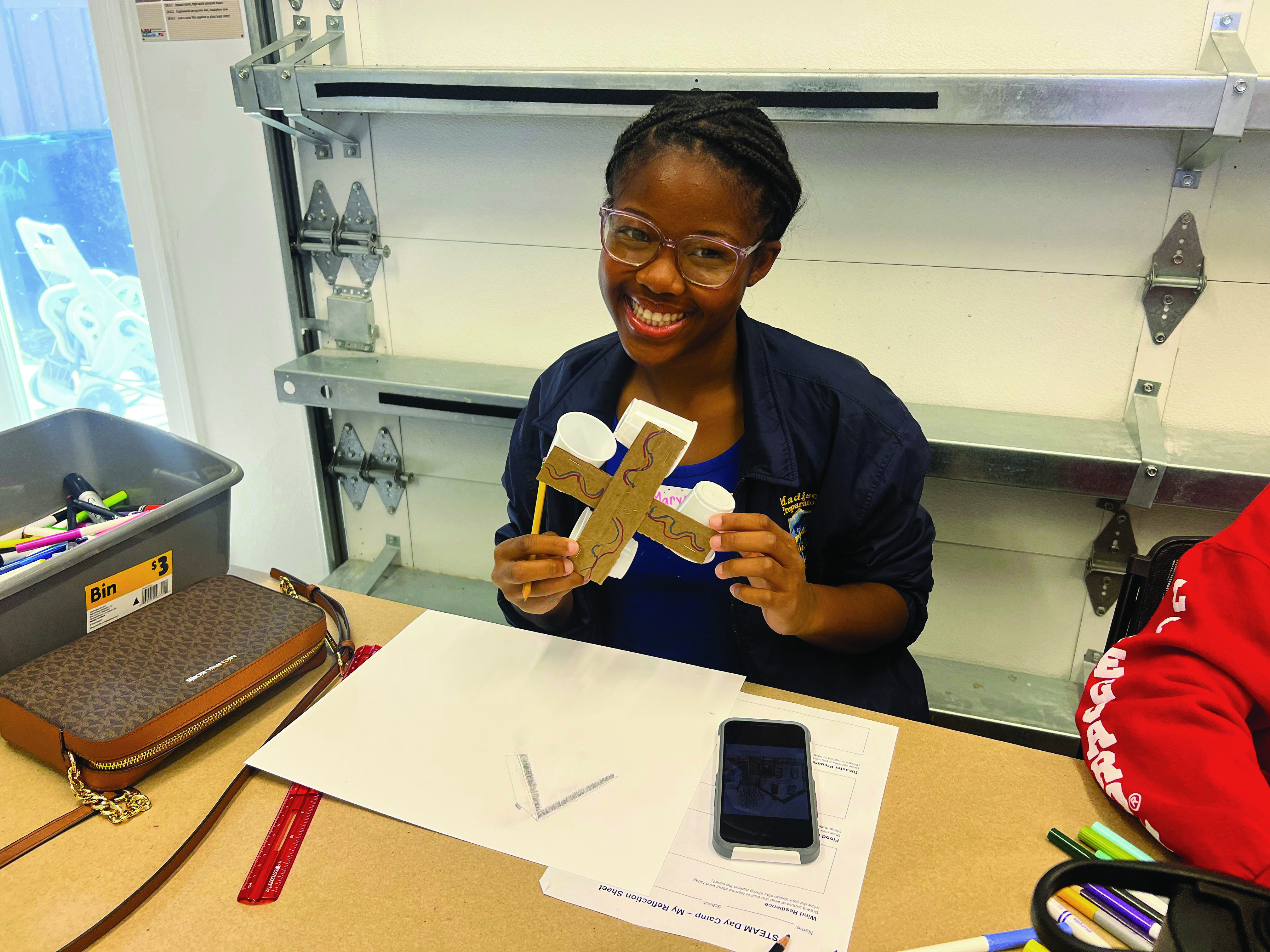 A girl creates a T-shaped wind-measuring instrument while sitting at a school desk.